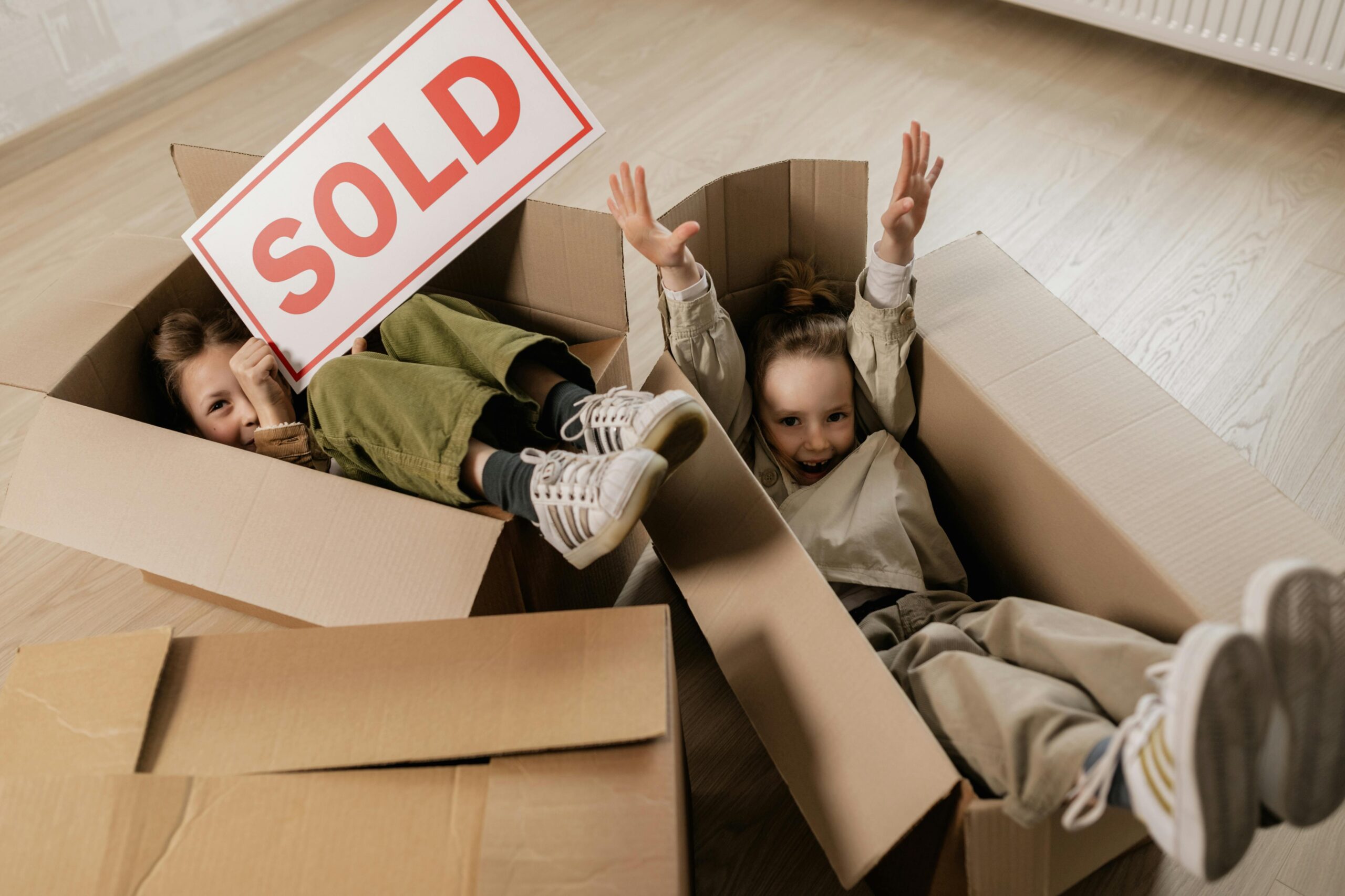 kids playing in boxes while moving with a sold sign in hands